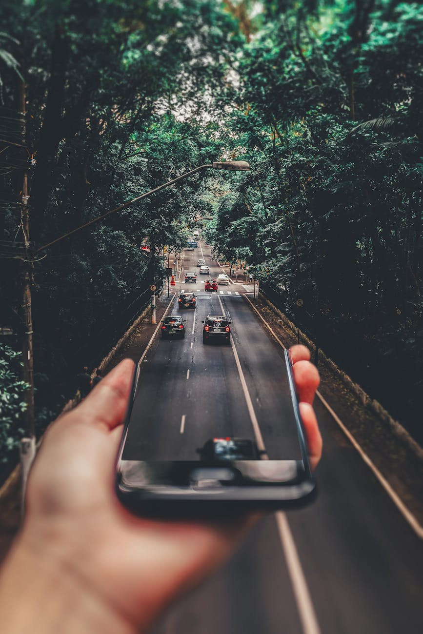 forced perspective photography of cars running on road below smartphone